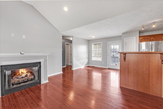 unfurnished living room featuring a textured ceiling, a lit fireplace, lofted ceiling, and wood-type flooring