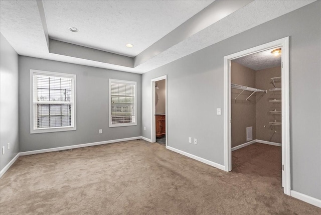 unfurnished bedroom featuring carpet flooring, a textured ceiling, visible vents, baseboards, and a spacious closet