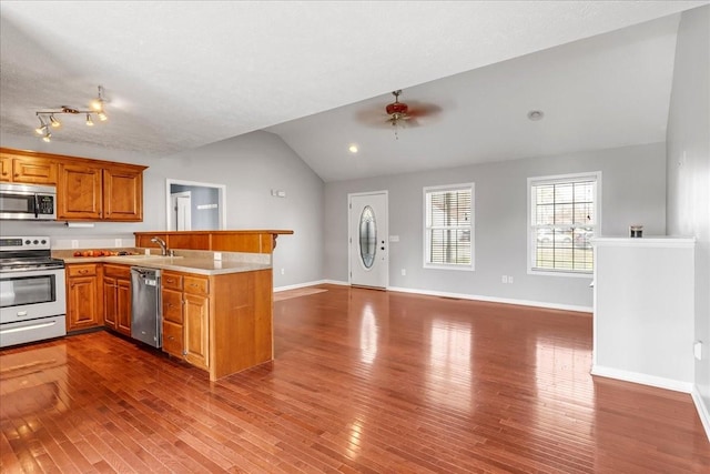kitchen featuring a peninsula, brown cabinets, stainless steel appliances, a ceiling fan, and vaulted ceiling