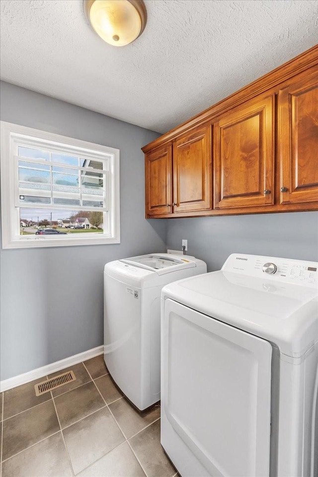 clothes washing area featuring tile patterned floors, a textured ceiling, independent washer and dryer, visible vents, and cabinet space
