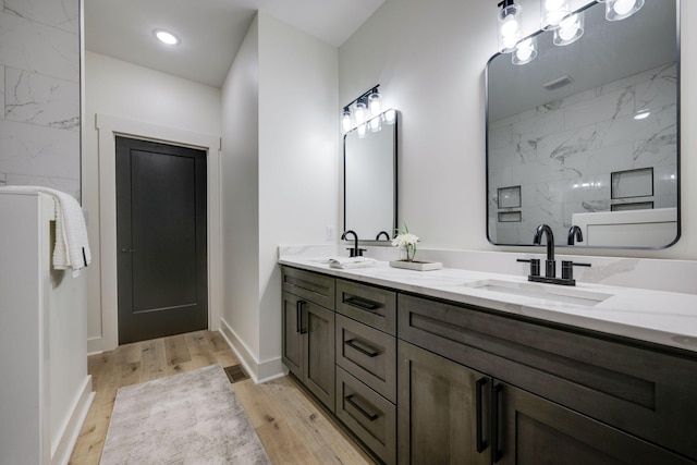 bathroom featuring double vanity, a sink, a marble finish shower, and wood finished floors