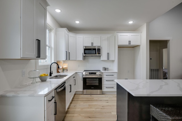 kitchen with white cabinets, light wood finished floors, light stone countertops, stainless steel appliances, and a sink