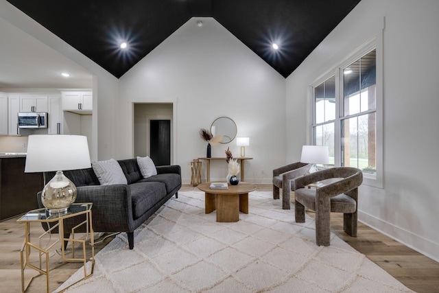 living area featuring baseboards, high vaulted ceiling, light wood-style flooring, and recessed lighting