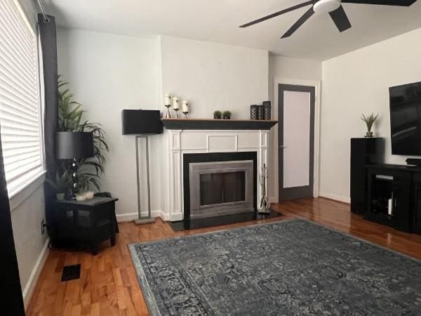 living area featuring ceiling fan, wood finished floors, a fireplace with flush hearth, and baseboards