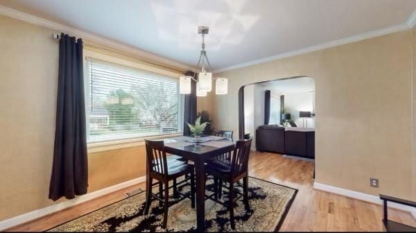 dining area featuring arched walkways, wood finished floors, baseboards, and ornamental molding