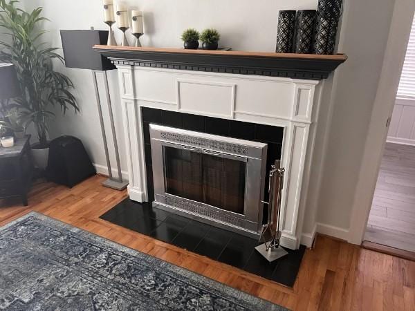 detailed view of a fireplace, wood finished floors, and baseboards