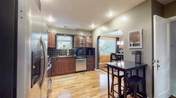 kitchen featuring appliances with stainless steel finishes, arched walkways, plenty of natural light, light wood-type flooring, and recessed lighting