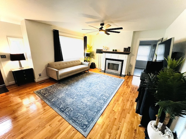 living area featuring ceiling fan, light wood-style flooring, and a fireplace with flush hearth