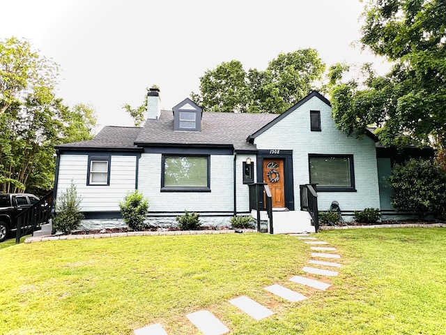 view of front of house featuring a chimney, a front lawn, roof with shingles, and brick siding
