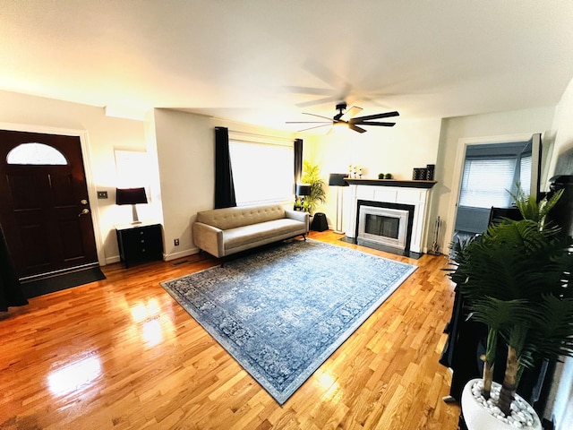 living room featuring a fireplace with flush hearth, light wood-style floors, a ceiling fan, and healthy amount of natural light