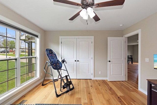 exercise room with baseboards, light wood-type flooring, and ceiling fan