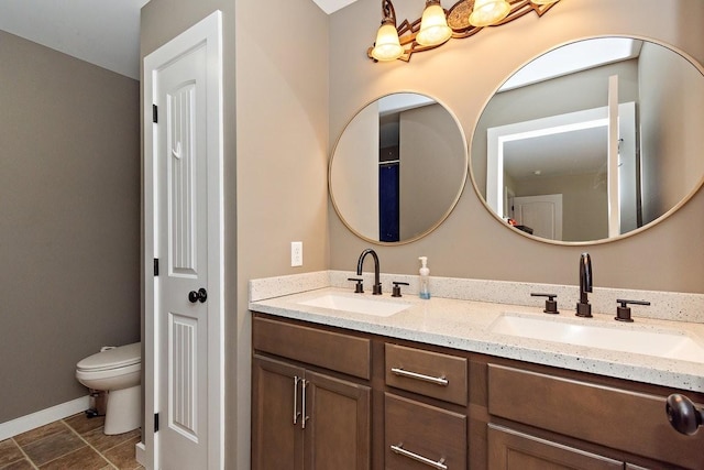 bathroom with double vanity, a sink, toilet, and baseboards
