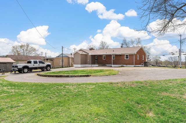 exterior space with central AC unit, driveway, brick siding, and a yard