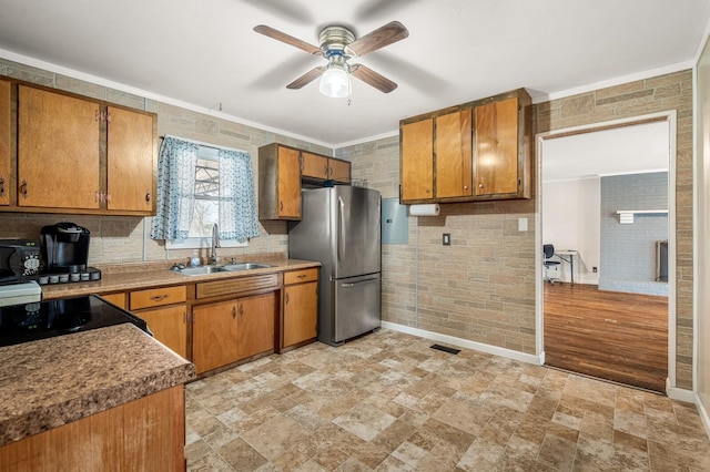 kitchen with ornamental molding, brown cabinets, a ceiling fan, a sink, and freestanding refrigerator