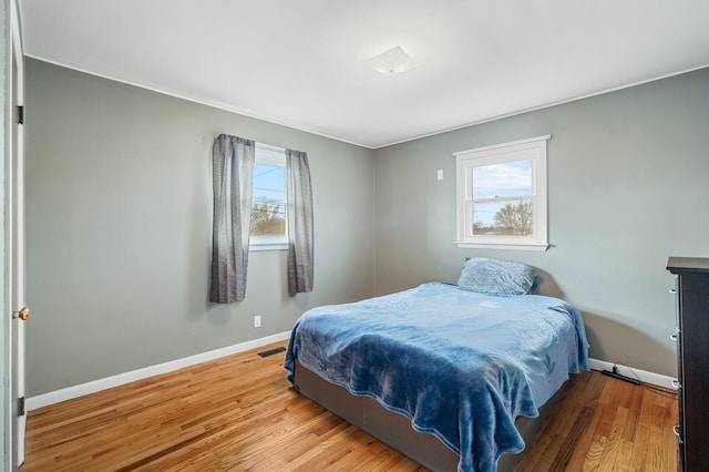 bedroom with baseboards, visible vents, multiple windows, and wood finished floors