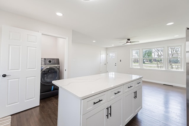 kitchen with washer / clothes dryer, ceiling fan, dark wood finished floors, light stone countertops, and a kitchen island