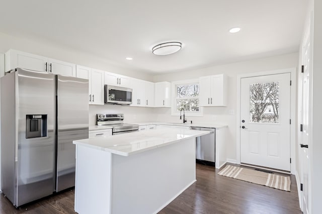 kitchen featuring white cabinets, a center island, appliances with stainless steel finishes, dark wood-style flooring, and a sink