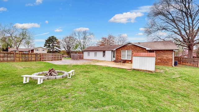 rear view of house with an outdoor structure, a patio, a fenced backyard, an outdoor fire pit, and a lawn