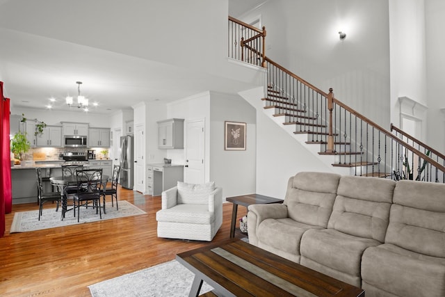 living room featuring ornamental molding, stairway, light wood-type flooring, a high ceiling, and an inviting chandelier