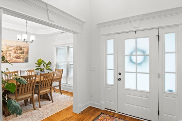entrance foyer with baseboards, light wood-type flooring, ornamental molding, and an inviting chandelier