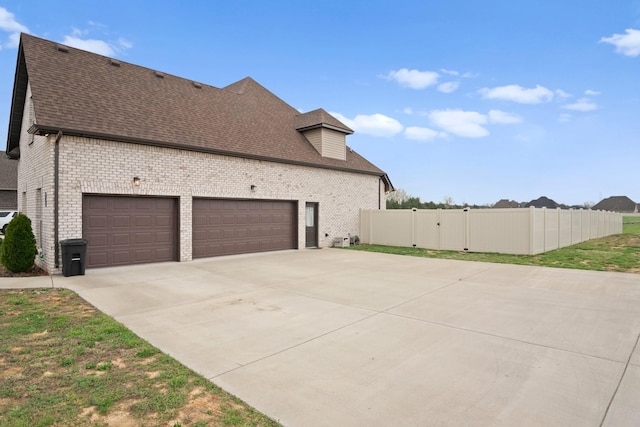 view of side of home featuring roof with shingles, driveway, a gate, brick siding, and a garage