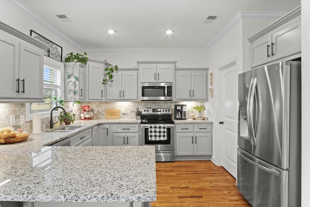 kitchen with crown molding, a sink, appliances with stainless steel finishes, a peninsula, and visible vents