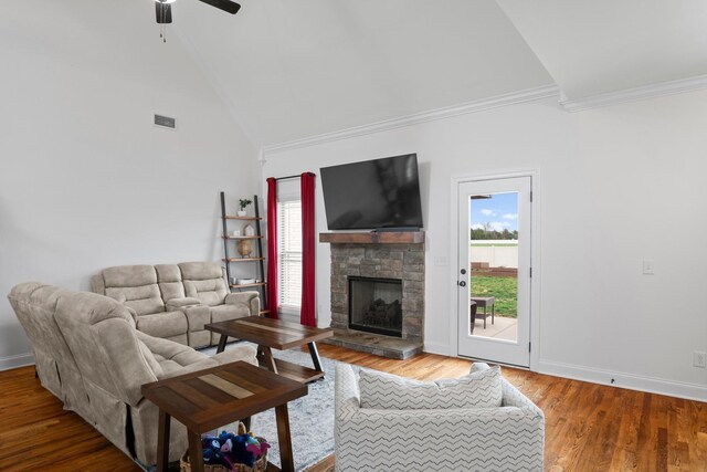 living area featuring a ceiling fan, wood finished floors, a stone fireplace, visible vents, and ornamental molding