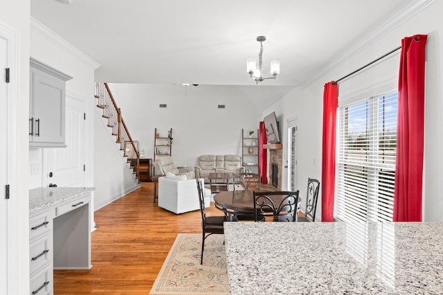 dining area with crown molding, lofted ceiling, stairs, a chandelier, and light wood-style flooring