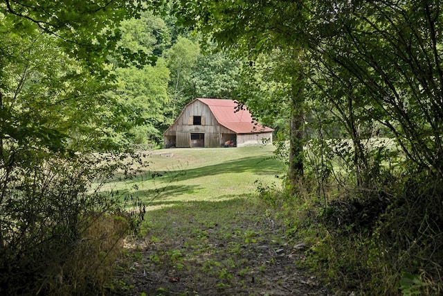 view of yard featuring an outbuilding, a forest view, a barn, and a detached garage