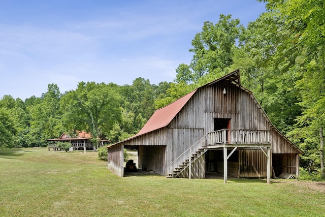rear view of property with a wooded view, an outdoor structure, a barn, and a yard