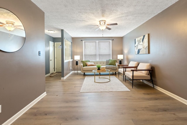 living area with baseboards, a textured ceiling, wood finished floors, and a ceiling fan