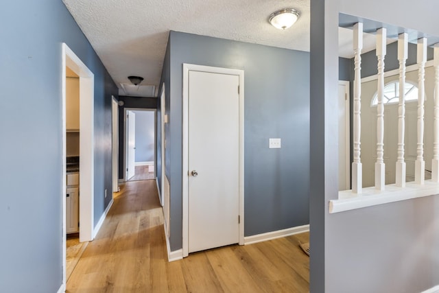hall with baseboards, light wood-style floors, and a textured ceiling