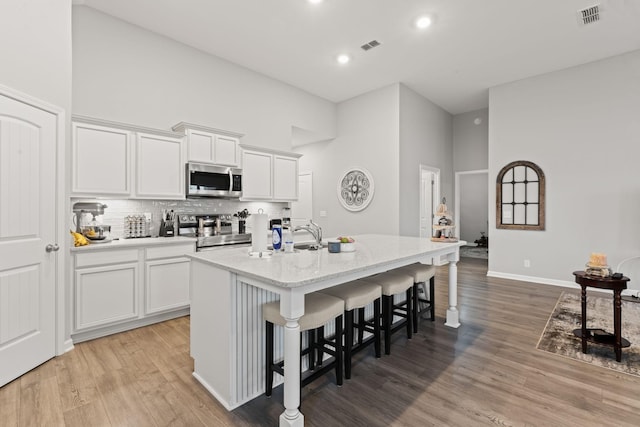 kitchen with tasteful backsplash, a kitchen bar, light wood finished floors, a center island with sink, and stainless steel appliances