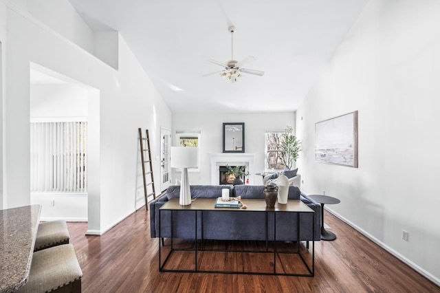 office area with a premium fireplace, lofted ceiling, baseboards, ceiling fan, and dark wood-style flooring