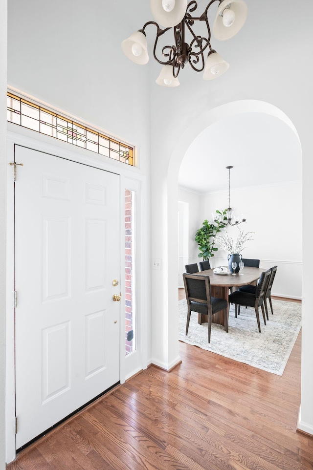 entryway featuring arched walkways, baseboards, wood finished floors, and an inviting chandelier