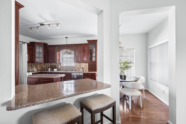 kitchen with a kitchen breakfast bar, dark wood finished floors, backsplash, appliances with stainless steel finishes, and glass insert cabinets
