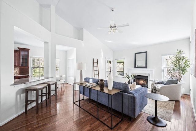 living area with a premium fireplace, high vaulted ceiling, baseboards, dark wood-style floors, and a ceiling fan