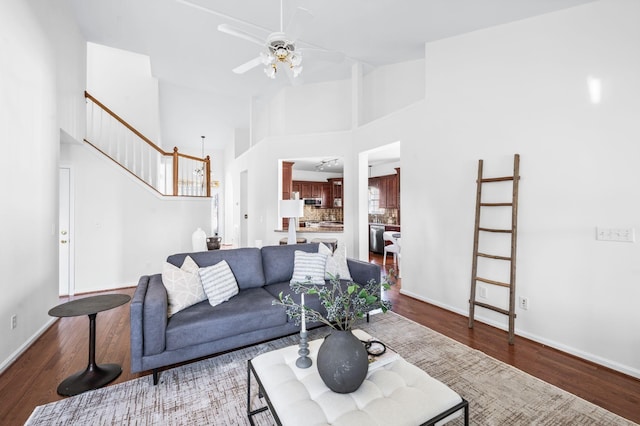 living room with a ceiling fan, dark wood-type flooring, stairway, and baseboards