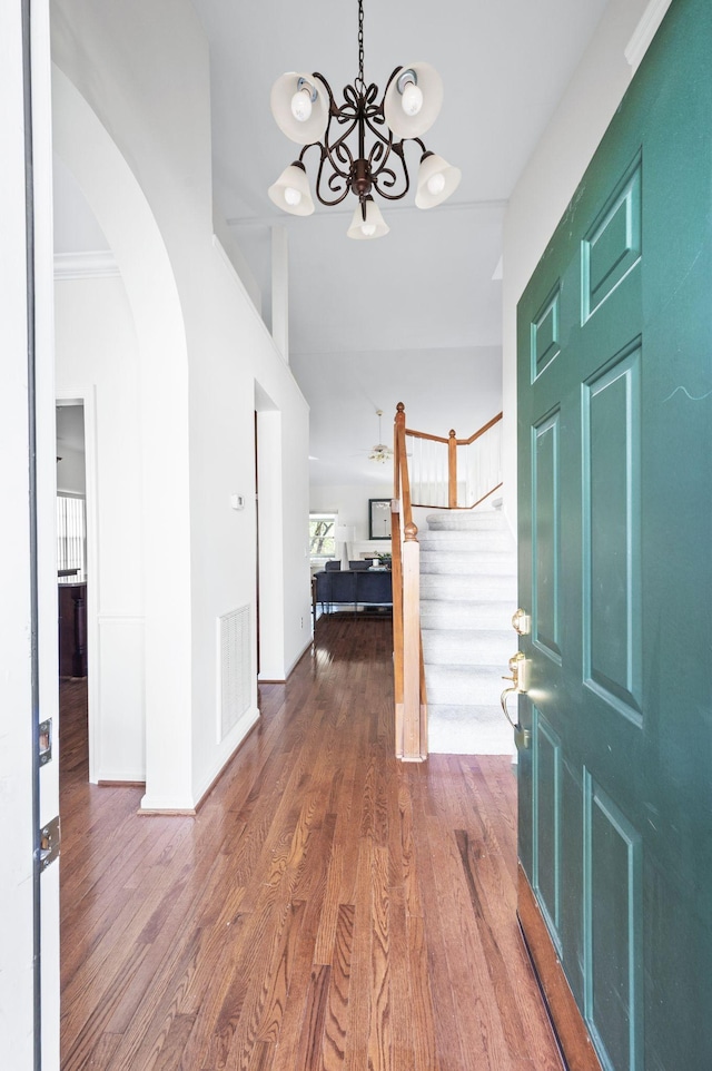 entrance foyer with stairs, a chandelier, wood finished floors, visible vents, and arched walkways