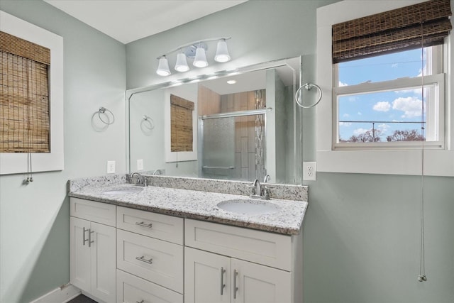 full bathroom with baseboards, double vanity, a sink, and a stall shower