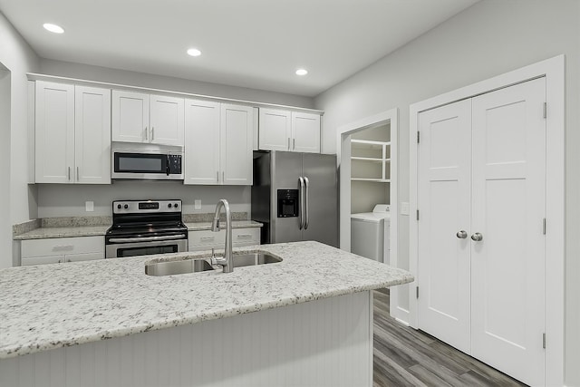 kitchen featuring wood finished floors, appliances with stainless steel finishes, white cabinetry, a sink, and washer and dryer