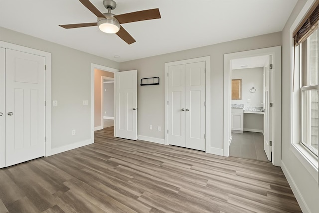unfurnished bedroom with ensuite bathroom, baseboards, light wood-style floors, a ceiling fan, and a closet