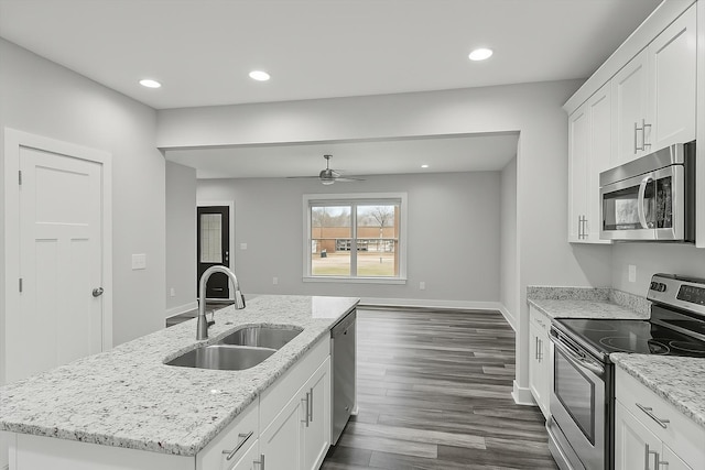 kitchen with dark wood-style flooring, stainless steel appliances, a center island with sink, a sink, and a ceiling fan