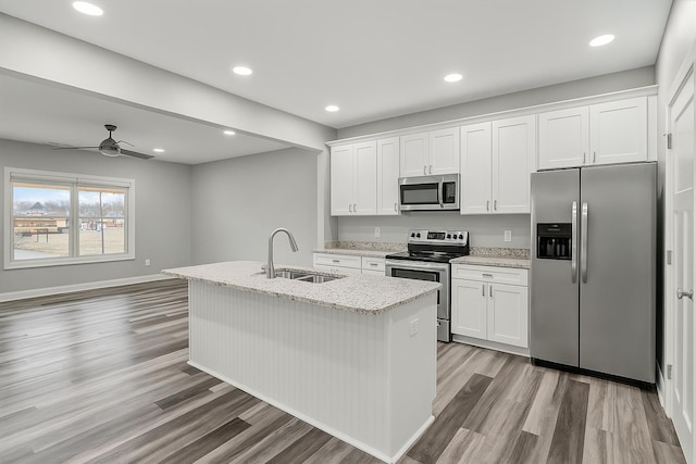 kitchen with white cabinetry, light wood-type flooring, a center island with sink, a sink, and appliances with stainless steel finishes