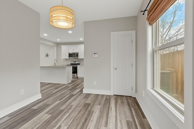 unfurnished living room featuring light wood-style flooring, a sink, baseboards, and recessed lighting