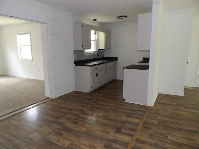 kitchen featuring dark wood-style flooring, ornamental molding, dark countertops, a sink, and backsplash
