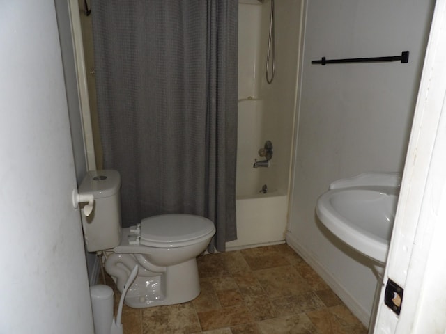 bathroom featuring stone finish floor, toilet, a sink, and shower / bath combo