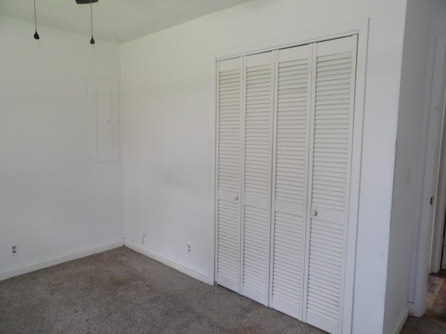 unfurnished bedroom with a closet, baseboards, electric panel, and carpet