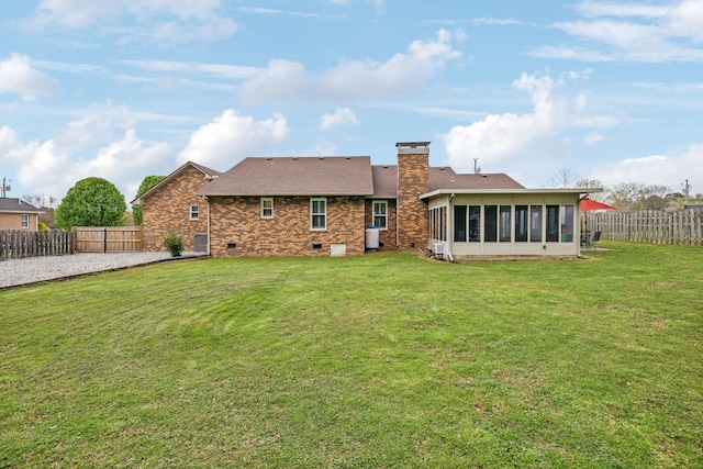 rear view of house with a chimney, a sunroom, a fenced backyard, and a yard