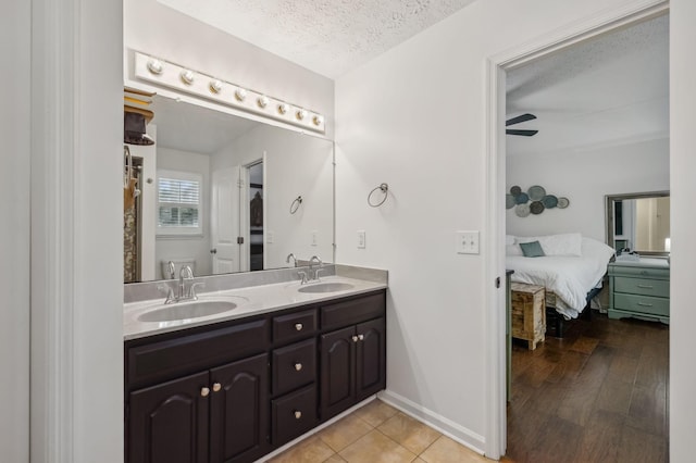 ensuite bathroom featuring double vanity, a sink, connected bathroom, and a textured ceiling